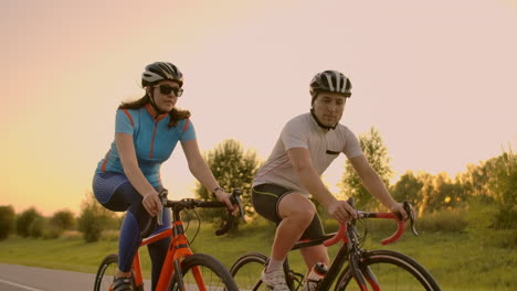 Two-professional-road-cyclists-ride-their-bikes-on-a-hill.-Hand-held-shot-of-two-strong-cyclists-female-and-male-on-their-training-on-a-warm-but-windy-summer-day